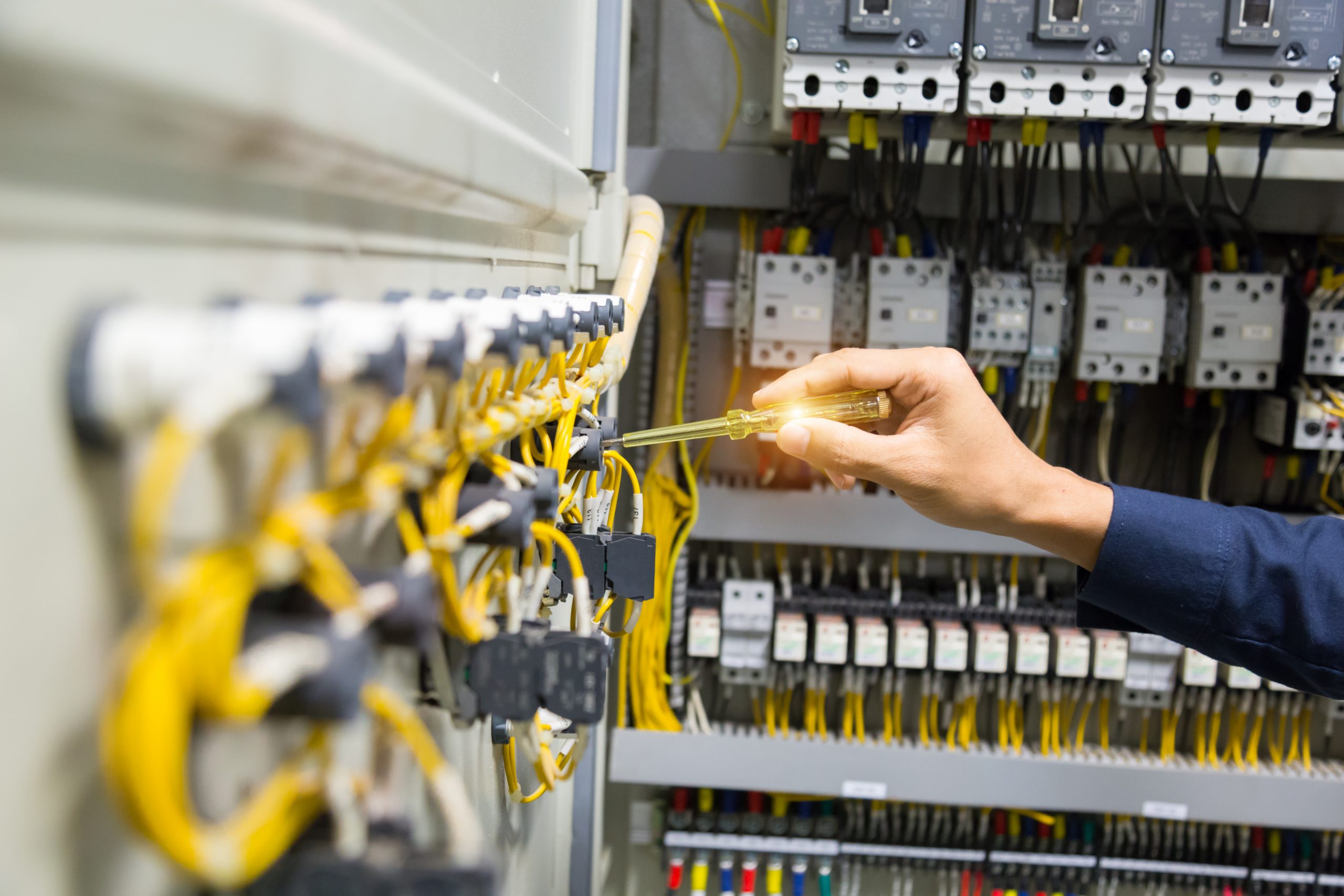 Electricians hands testing current electric in control panel.